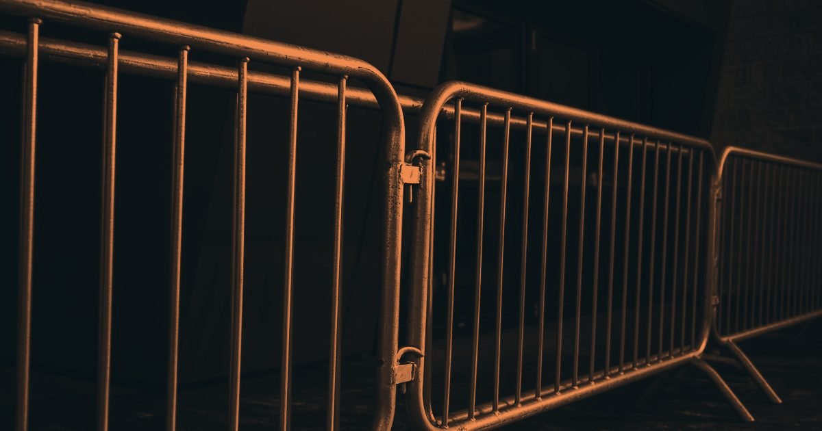 Steel crowd barriers lined up at night in a charcoal and orange duotone